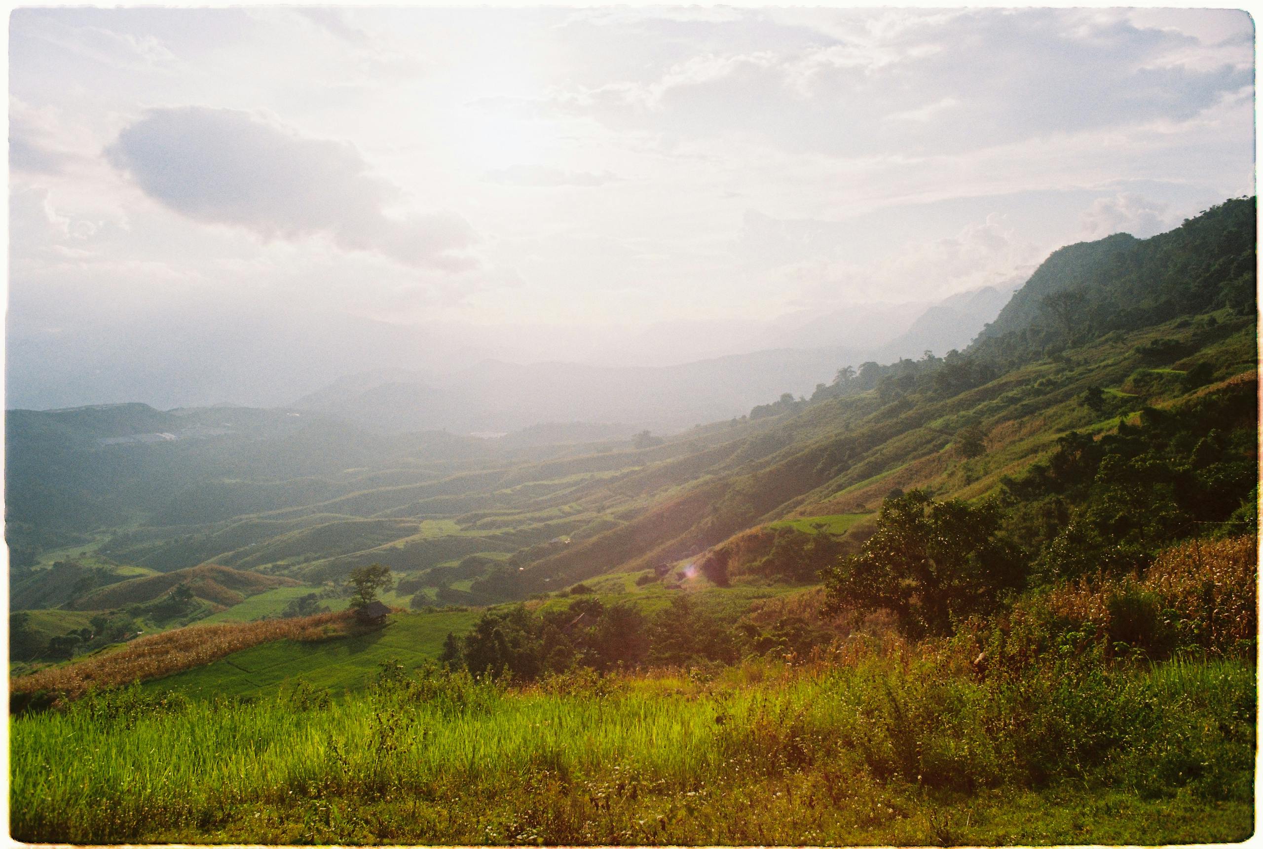 Breathtaking view of rolling hills and mountains under a serene sunset light.
