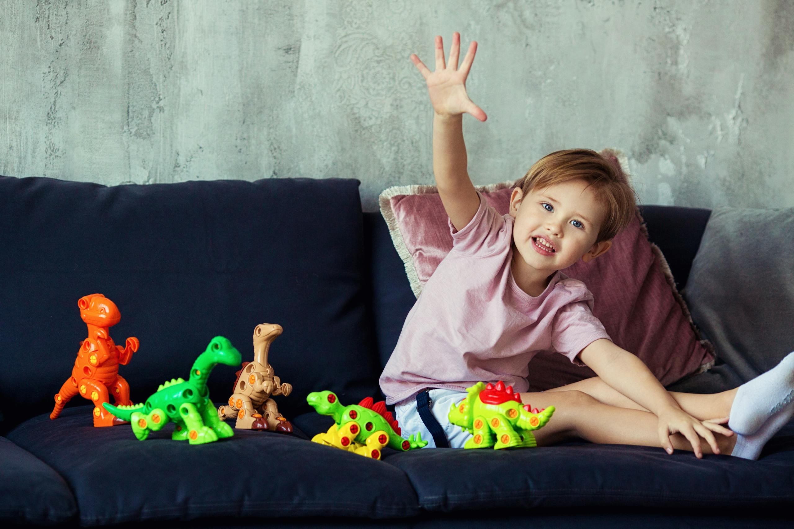 Happy child sitting on sofa playing with colorful dinosaur toys indoors.
