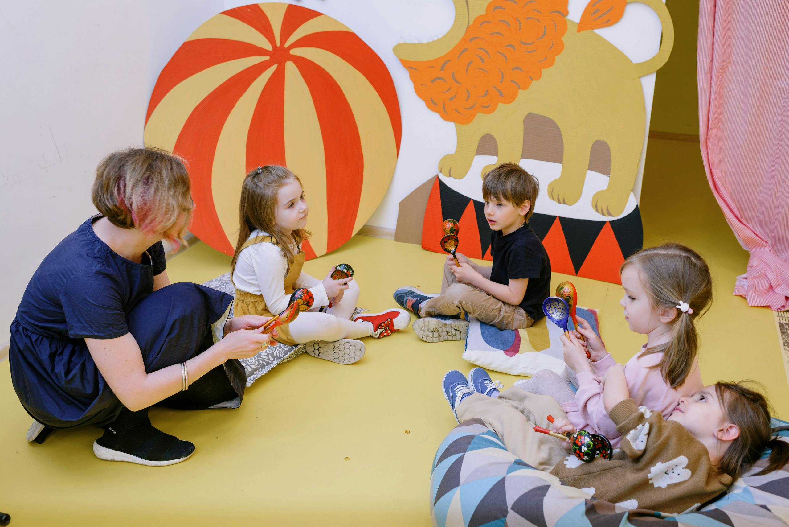 Kids playing with maracas in a colorful playroom with a teacher.